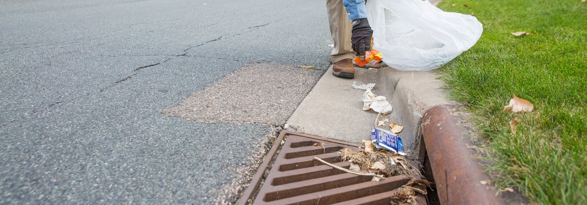 A man picks up trash and other debris from a storm drain located on a residential street