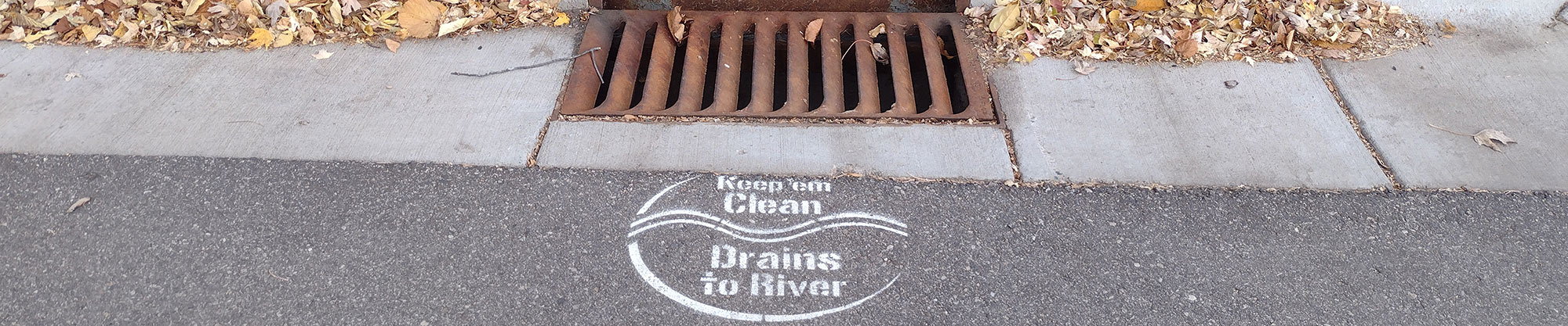 Storm drain with text "Keep 'em clean. Drains to river."